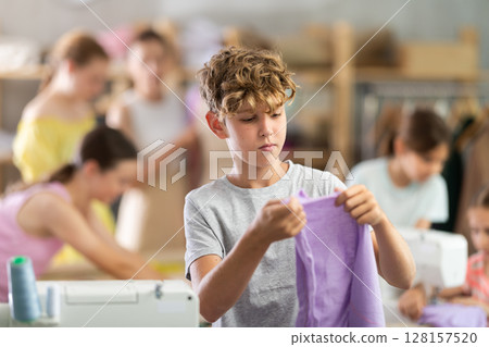 Boy checking stitched fabric at school sewing workshop 128157520