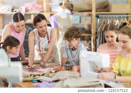Sewing lesson - a group of teenage children learn to sew on sewing machine and cut fabric 128157522