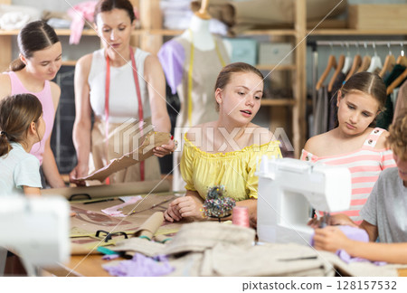 Teen girl watching peer sewing at machine during class Teen girl watching peer sewing at machine during class 128157532