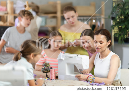 Seamstress explaining sewing techniques to schoolchildren in training workshop 128157595