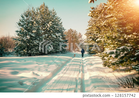 Man and dog are best friends. A man and a dog on a leash walk along a country road covered with snow 128157742