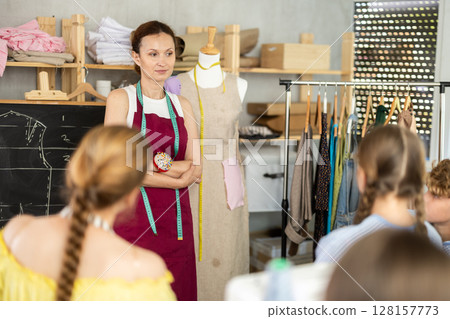 Woman teacher at blackboard conducts theoretical lesson for sewing school children students 128157773