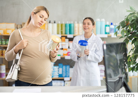 Expecting mother checking baby formula label while pharmacist offering alternative 128157775
