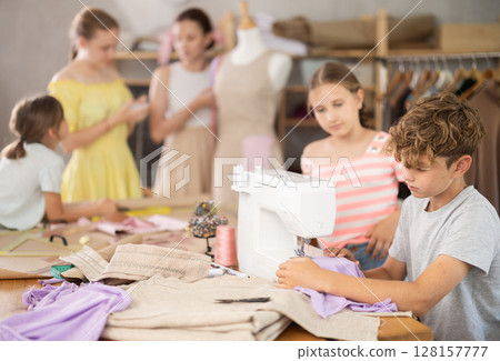 Girl child watches male classmates sew and creating clothes Girl child watches male classmates sew and creating clothes 128157777