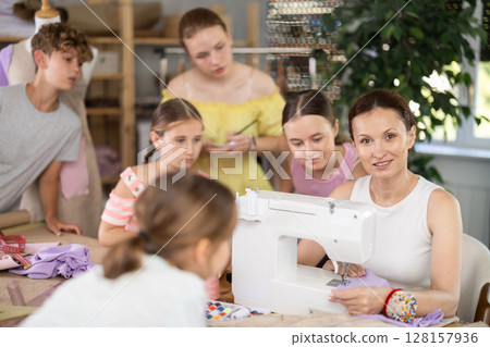Female instructor demonstrating stitching at machine to teenage students Female instructor demonstrating stitching at machine to teenage students 128157936