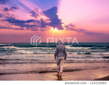 Seascape in the evening with a beautiful sky. A man walks barefoot on the beach and looks at a magical sunset Seascape in the evening with a beautiful sky. A man walks barefoot on the beach and looks at a magical sunset 128158064