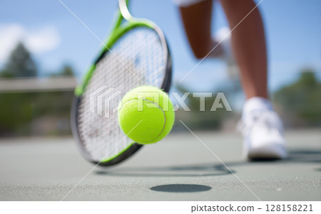 Tennis ball in midair close to racket on outdoor court with player in white shoes and shorts, capturing dynamic sports action and focus on ball movement 128158221