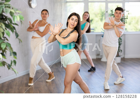 Ordinary teen girls and boy performing kick step movement during training together in dance studio 128158228