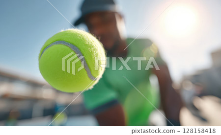 Tennis ball in sharp focus with blurred tennis player in green shirt and cap hitting forehand stroke under bright sunlight on outdoor court Tennis ball in sharp focus with blurred tennis player in green shirt and cap hitting forehand stroke under bright sunlight on outdoor court 128158418