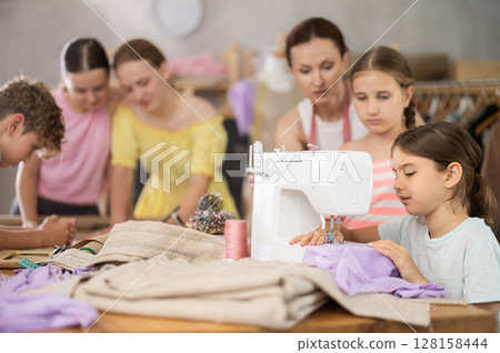 Woman teacher oversees teen girl childs work on sewing machine 128158444