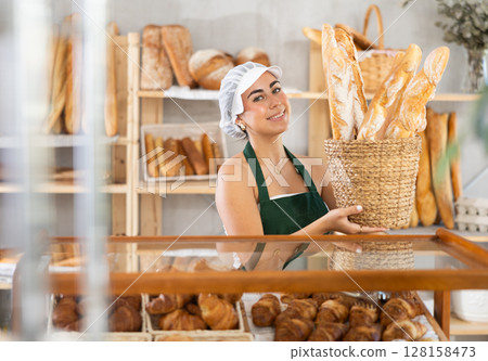 Young saleswoman displays baguettes in wicker basket Young saleswoman displays baguettes in wicker basket 128158473