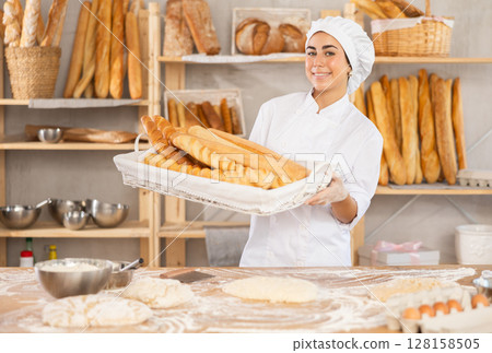 Young female baker with basket of baguettes 128158505