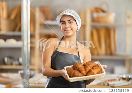 Young saleswoman displays croissants in square wicker basket Young saleswoman displays croissants in square wicker basket 128158539