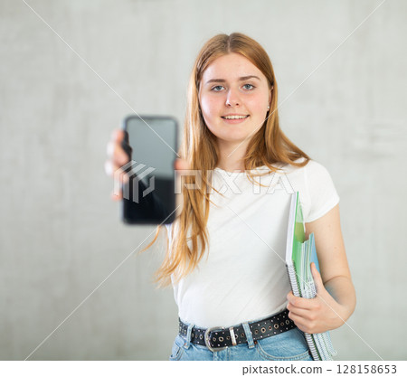 Young girl student showing modern smart phone with blank screen Young girl student showing modern smart phone with blank screen 128158653