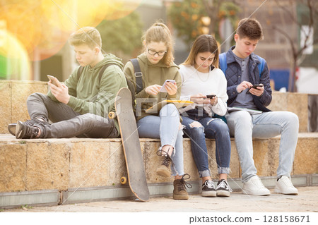 Group of teens using smartphones outdoors Group of teens using smartphones outdoors 128158671