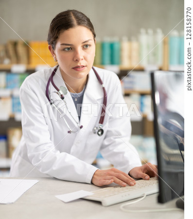 Young female pharmacist working with computer in chemist's shop 128158770