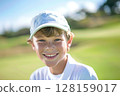 Happy caucasian boy at golfing training lesson, smiling at the camera on a sunny golf course, surrounded by lush green fairways and practicing his swing with enthusiasm, enjoying the sport and 128159017