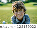 Caucasian boy at a golf training session, happily looking at the camera on a vibrant golf course, engaging in his lesson with eagerness, highlighting the fun and educational aspects of the sport for 128159022