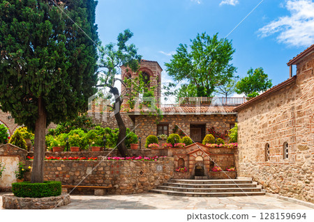 Peaceful monastery courtyard with stone fountain and blooming flowers in Meteora Greece 128159694