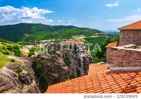 Elevated perspective over orange tiles toward Meteora monasteries on vertical cliffs in Greece 128159695