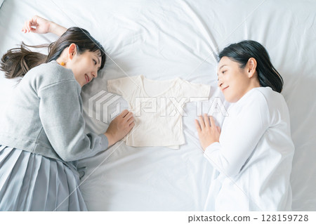Mother and daughter lying on the bed, holding each other's underwear, eagerly waiting for the baby 128159728