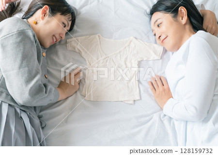 Mother and daughter lying on the bed, holding each other's underwear, eagerly waiting for the baby Mother and daughter lying on the bed, holding each other's underwear, eagerly waiting for the baby 128159732