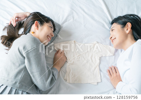 Mother and daughter lying on the bed, holding each other's underwear, eagerly waiting for the baby 128159756