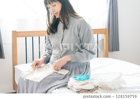 Pregnant woman preparing baby clothes in bedroom 128159759