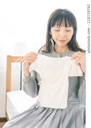 Pregnant woman preparing baby clothes in bedroom 128159762