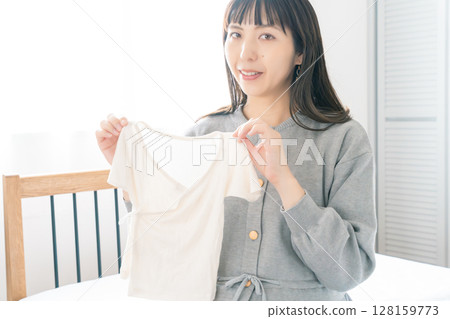 Pregnant woman preparing baby clothes in bedroom Pregnant woman preparing baby clothes in bedroom 128159773