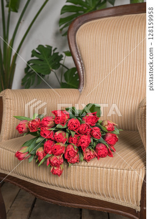 Bouquet of red tulips on a striped armchair in a cozy setting with greenery Bouquet of red tulips on a striped armchair in a cozy setting with greenery 128159958