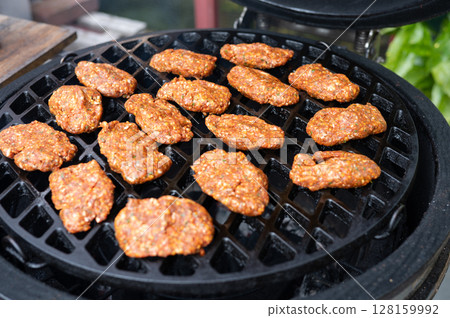 Spicy homemade sausage patties grilling on open flame bbq grill outdoors Spicy homemade sausage patties grilling on open flame bbq grill outdoors 128159992