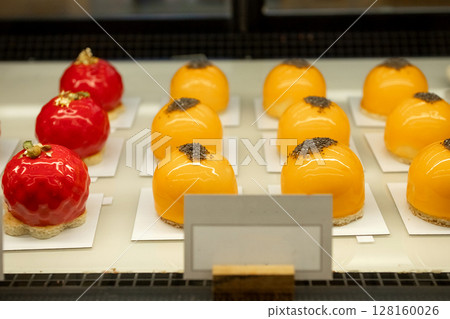 Orange and red dome-shaped pastries with glossy glaze on display. 128160026