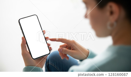 Woman holding and pointing at smartphone with blank screen, over shoulder view of person using mobile phone with empty display mockup 128160087