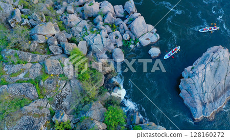 Aerial view of two kayaks navigating through a narrow rocky river pass surrounded by large boulders and lush vegetation in a scenic natural landscape 128160272