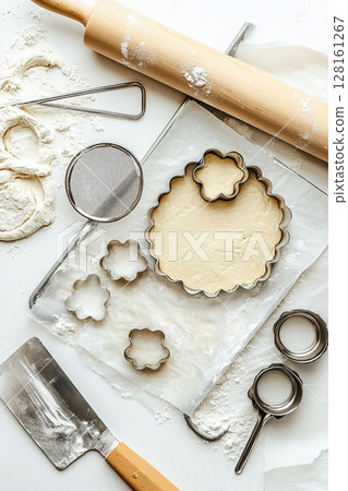 Top-down macro food photography style image of essential tools for baking perfect cut-out cookies, including metal cookie cutters, adjustable rolling pin with guide rings, baking sheet lined with 128161267
