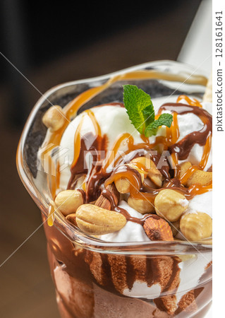 A delicious ice cream sundae topped with caramel sauce, chocolate syrup, nuts, wafer sticks, and a sprig of mint served in a glass cup A delicious ice cream sundae topped with caramel sauce, chocolate syrup, nuts, wafer sticks, and a sprig of mint served in a glass cup 128161641
