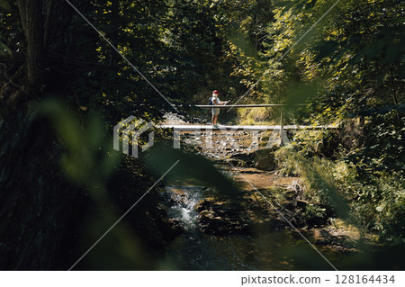 Person Standing on Small Bridge in Lush Forest Person Standing on Small Bridge in Lush Forest 128164434