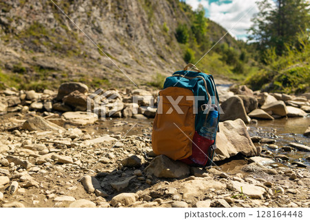 Backpack Standing on Rocky Riverbed in Mountain Valley Backpack Standing on Rocky Riverbed in Mountain Valley 128164448