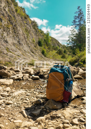 Backpack Standing on Rocky Riverbed in Mountain Valley 128164449