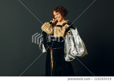 Portrait of a young adult woman dressed in a medieval dress holding shopping bags in hands Portrait of a young adult woman dressed in a medieval dress holding shopping bags in hands 128165019