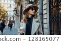 Stylish woman with coffee walks along a city street on a sunny autumn day in an urban setting 128165077