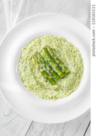 Asparagus risotto served in white plate with whole spears on top 128165211