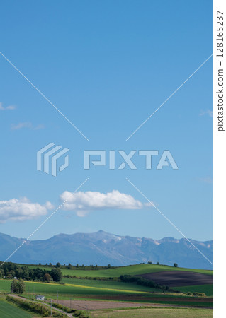 Hilly farmland and mountain ranges on a sunny summer day, Tokachi mountain range 128165237