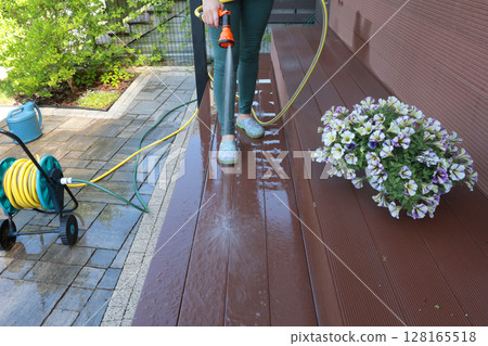 Anonymous cleaning, hose washing deck in summer. Structures in backyard. Clean and orderly. 128165518