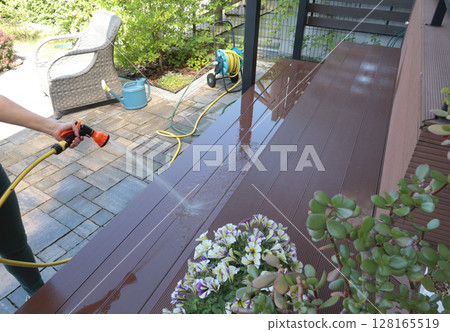 Anonymous cleaning, hose washing deck in summer. Structures in backyard. Clean and orderly. Anonymous cleaning, hose washing deck in summer. Structures in backyard. Clean and orderly. 128165519