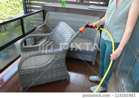 Anonymous cleaning, hosing wicker furniture in summer. Backyard buildings. Cleanliness and order. Anonymous cleaning, hosing wicker furniture in summer. Backyard buildings. Cleanliness and order. 128165981