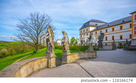 Visitors admire the impressive Baroque statues that adorn the grounds of the Kuks hospital complex in Czechia, showcasing intricate designs and historical significance against a scenic backdrop. 128166274