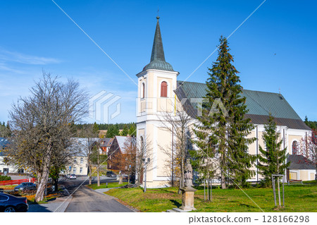 The historic Saint Anne Church in Bozi Dar showcases its elegant architecture under clear blue skies, surrounded by trees and charming buildings in the Ore Mountains of Czechia. The historic Saint Anne Church in Bozi Dar showcases its elegant architecture under clear blue skies, surrounded by trees and charming buildings in the Ore Mountains of Czechia. 128166298