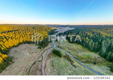 An overhead view of a road cutting through dense forest in the Krusne Mountains, casting long shadows during sunset. An overhead view of a road cutting through dense forest in the Krusne Mountains, casting long shadows during sunset. 128166302